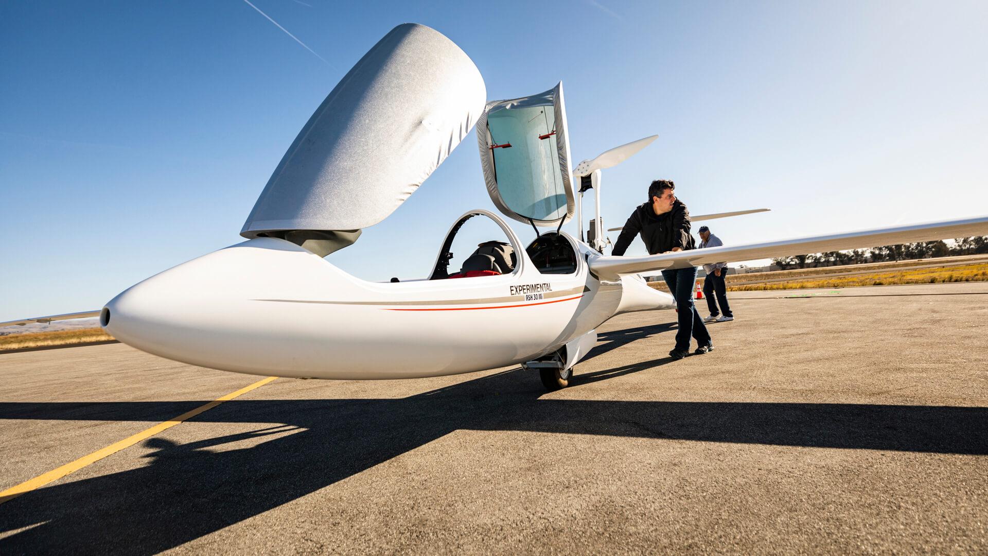 Student pushes a small experimental aircraft with open canopy on a runway during a hands-on aerospace engineering lab.