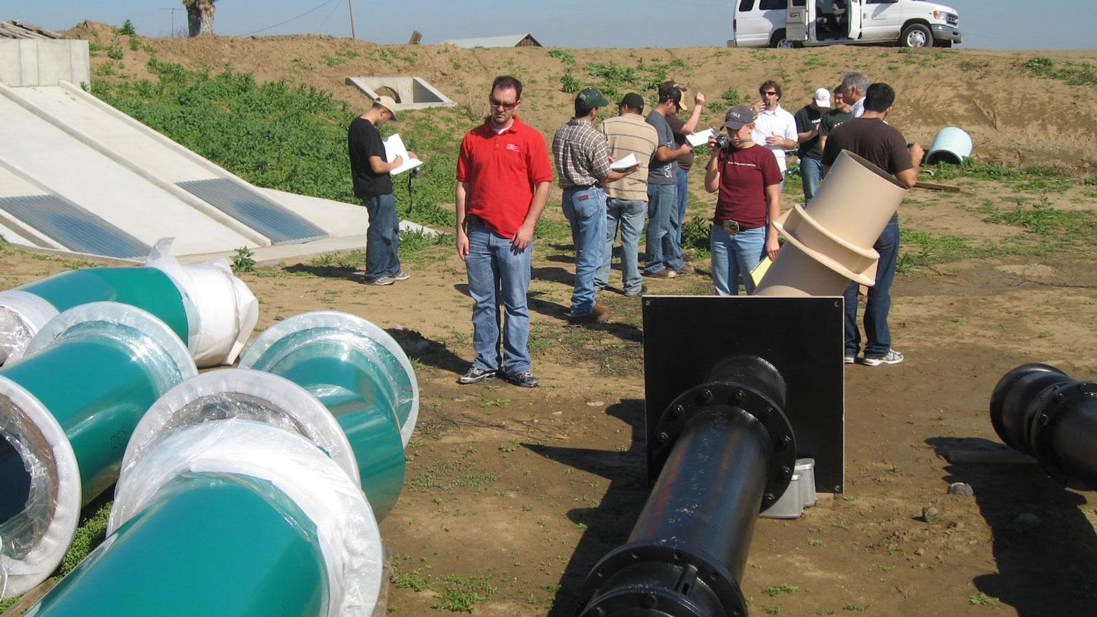 Group of students examining large irrigation pipes and drainage systems at an outdoor site.