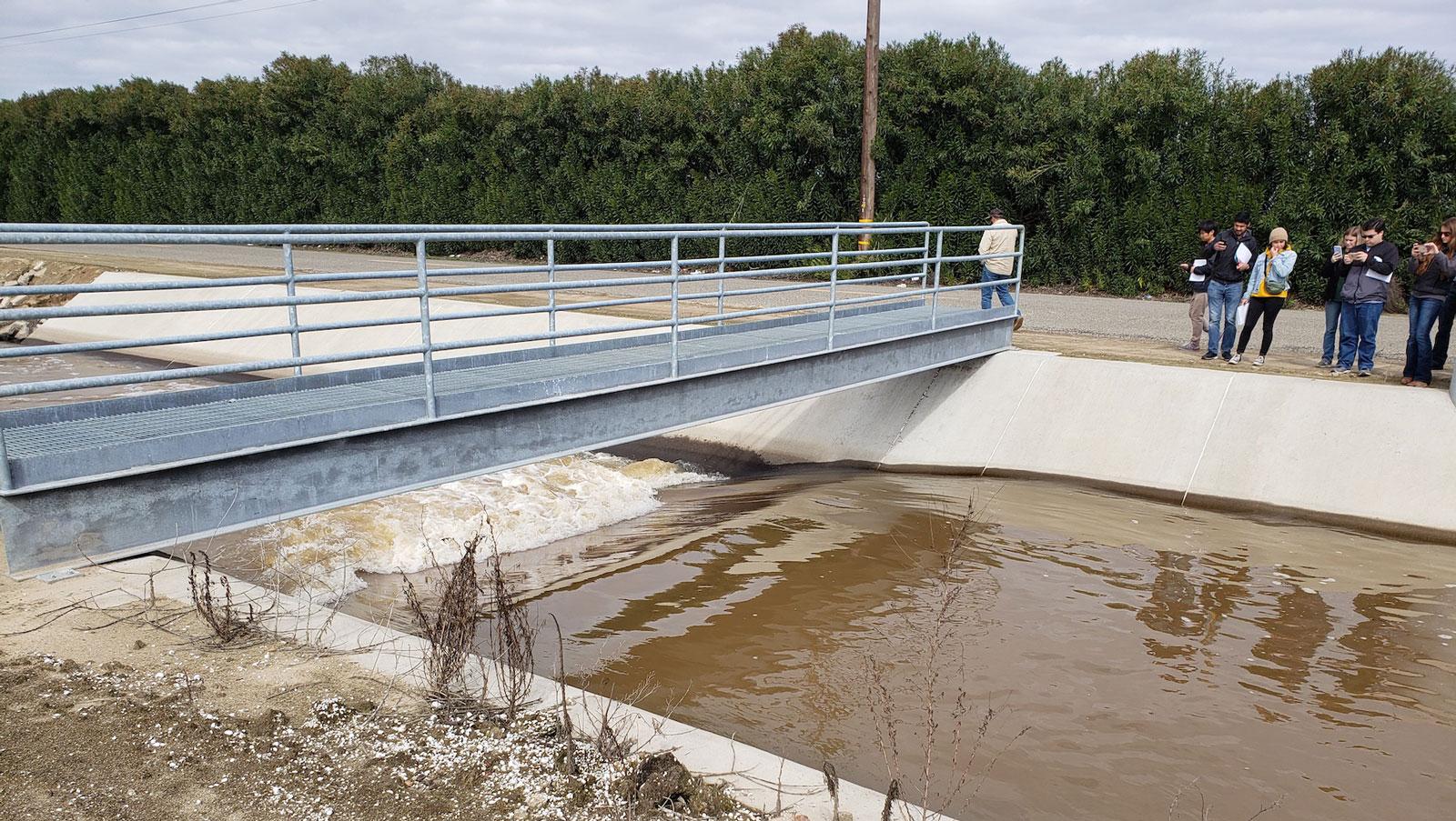 Students observing water flow beneath a small bridge at a concrete channel during a field site visit.