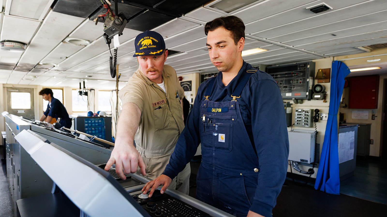 Instructor guides cadet on ship bridge during Cal Maritime training exercise.